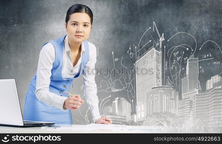 Businesswoman in process of work. Young attractive businesswoman working at her desk with laptop and construction project