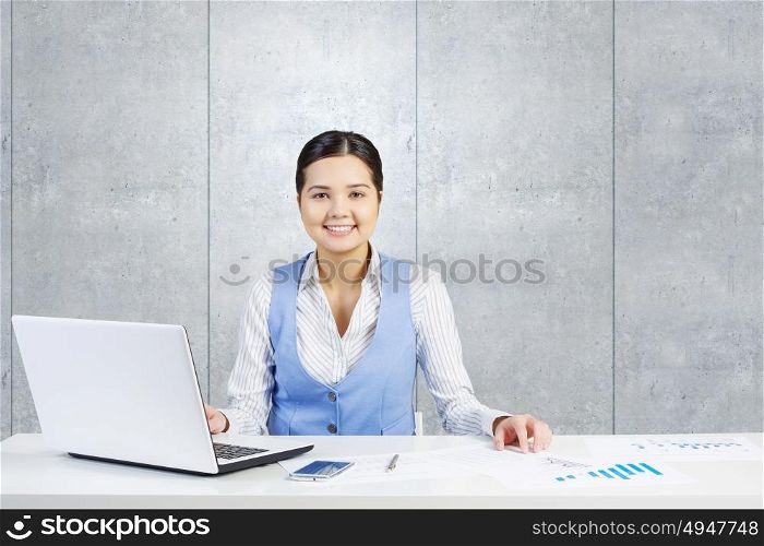 Businesswoman in process of work. Young attractive businesswoman working at her desk with laptop and papers