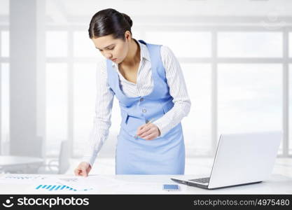 Businesswoman in process of work. Young attractive businesswoman working at her desk with laptop and papers