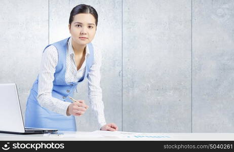 Businesswoman in process of work. Young attractive businesswoman working at her desk with laptop and papers