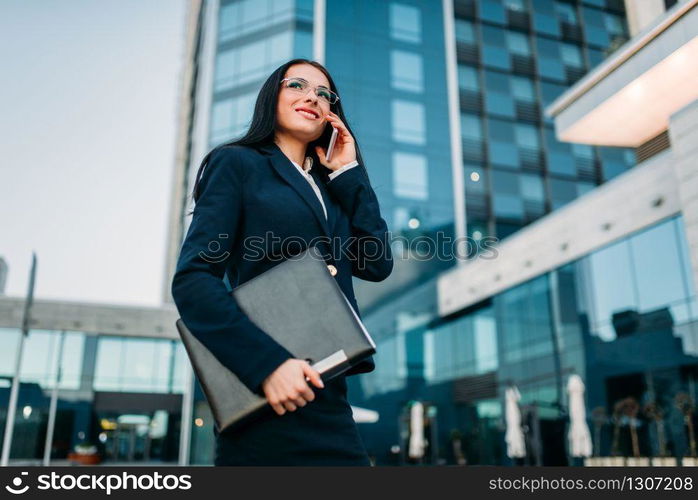 Businesswoman in suit talks by mobile phone outdoor, business center on background. Modern financial building. Successful female businessperson. Businesswoman in suit talks by phone outdoor