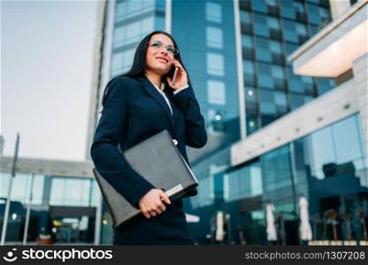 Businesswoman in suit talks by mobile phone outdoor, business center on background. Modern financial building. Successful female businessperson. Businesswoman in suit talks by phone outdoor