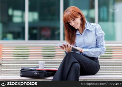 Businesswoman is sitting outside on a metal bank and working with a tablet pc