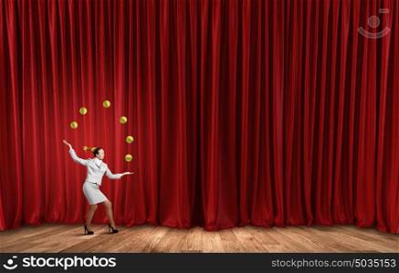 Businesswoman juggling with balls. Young businesswoman in cap on stage juggling with balls