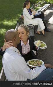 Businesswoman kissing a businessman with two business executives sitting in the background