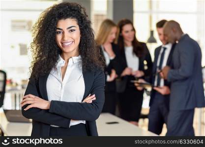 Businesswoman leader looking at camera in modern office with businesspeople working at the background. Teamwork concept. Muslim woman.