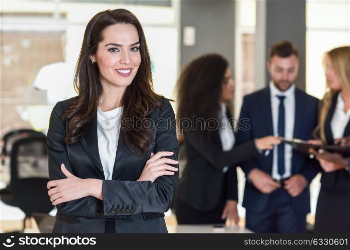 Businesswoman leader looking at camera in modern office with multi-ethnic businesspeople working at the background. Teamwork concept. Caucasian woman.