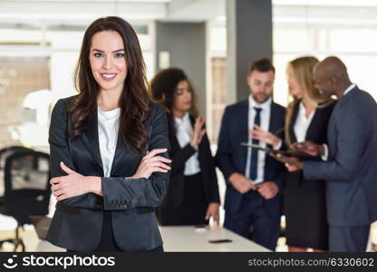 Businesswoman leader looking at camera in modern office with multi-ethnic businesspeople working at the background. Teamwork concept. Caucasian woman.