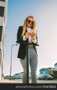 Businesswoman leaning on her electric scooter looking at the mobile in the street