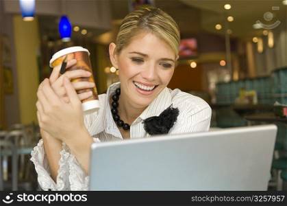 Businesswoman looking at a laptop and holding a disposable cup in a restaurant