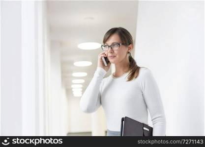 Businesswoman looking away while talking on smartphone in corridor at office