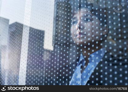 Businesswoman looking out through window, reflection of the city on the glass