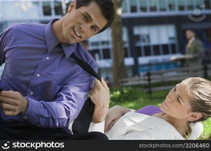 Businesswoman lying on grass and pulling the tie of a businessman