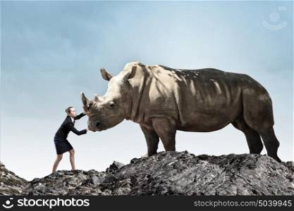 Businesswoman making effort to move huge rhino