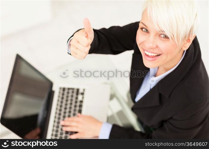 Businesswoman making positive thumb gesture while smiling in the office