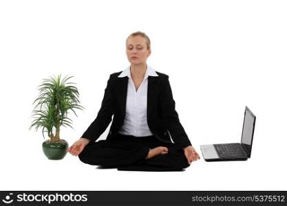 Businesswoman meditating next to laptop