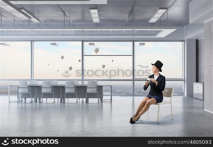 Businesswoman on chair in office. Elegant businesswoman in suit and hat sitting on chair in office interior