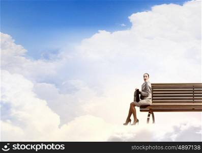 Businesswoman on cloud. Young businesswoman sitting on bench high in sky