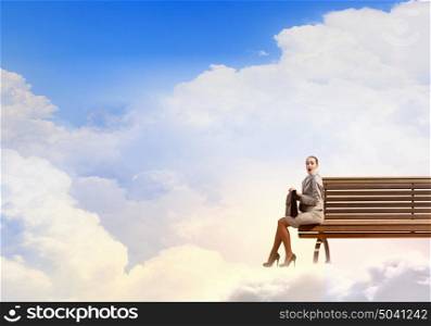 Businesswoman on cloud. Young businesswoman sitting on bench high in sky