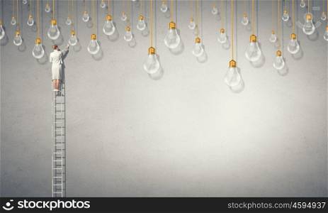 Businesswoman on ladder. Back view of businesswoman standing on ladder and reaching light bulb