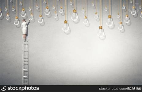 Businesswoman on ladder. Back view of businesswoman standing on ladder and reaching light bulb