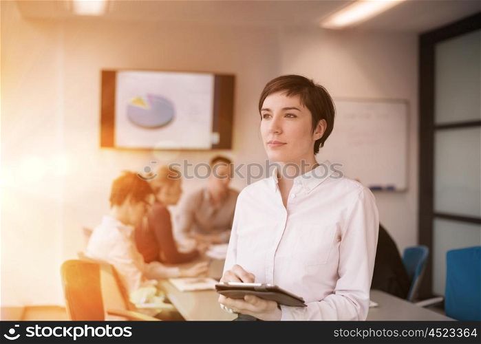businesswoman on meeting using tablet computer blured group of business people in background at modern bright startup office interior