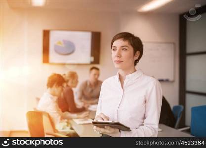 businesswoman on meeting using tablet computer blured group of business people in background at modern bright startup office interior