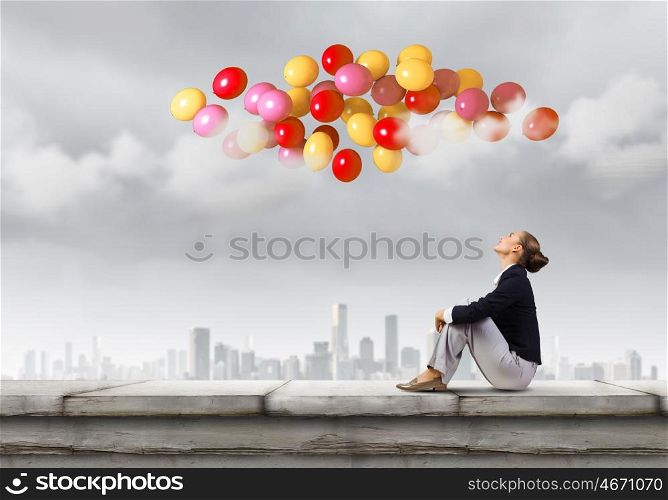 Businesswoman on roof. Young pretty businesswoman sitting on top of building with colorful balloons flying above