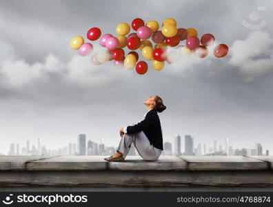 Businesswoman on roof. Young pretty businesswoman sitting on top of building with colorful balloons flying above