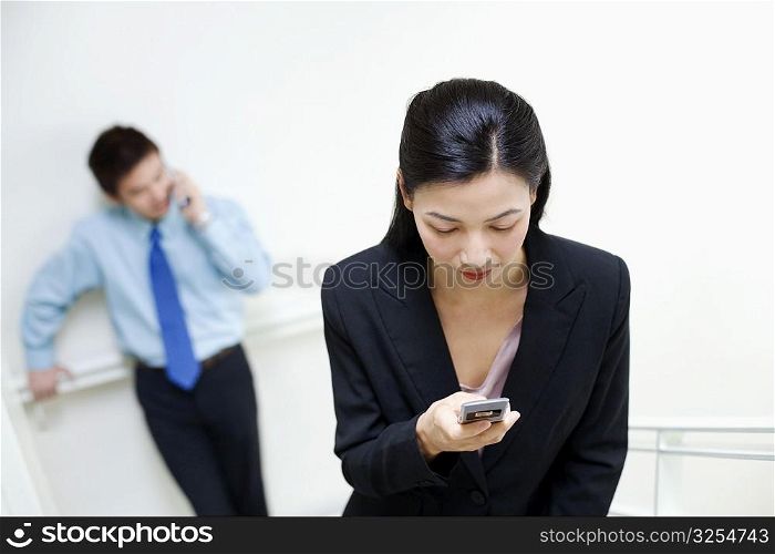 Businesswoman operating a mobile phone with a businessman standing behind her