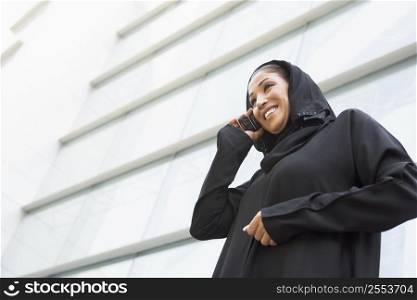 Businesswoman outdoors by building using cellular phone and smiling (selective focus)