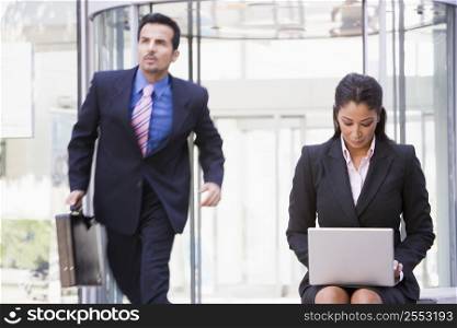 Businesswoman outdoors in front of building using laptop with businessman in background (high key/blur)