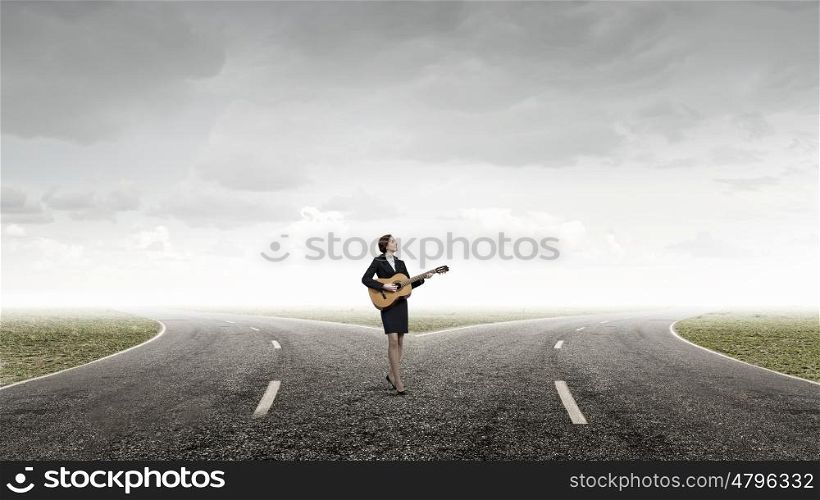 Businesswoman playing acoustic guitar. Cheerful businesswoman standing on road and playing acoustic guitar