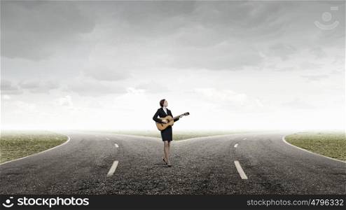 Businesswoman playing acoustic guitar. Cheerful businesswoman standing on road and playing acoustic guitar
