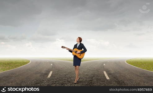 Businesswoman playing acoustic guitar. Cheerful businesswoman standing on road and playing acoustic guitar