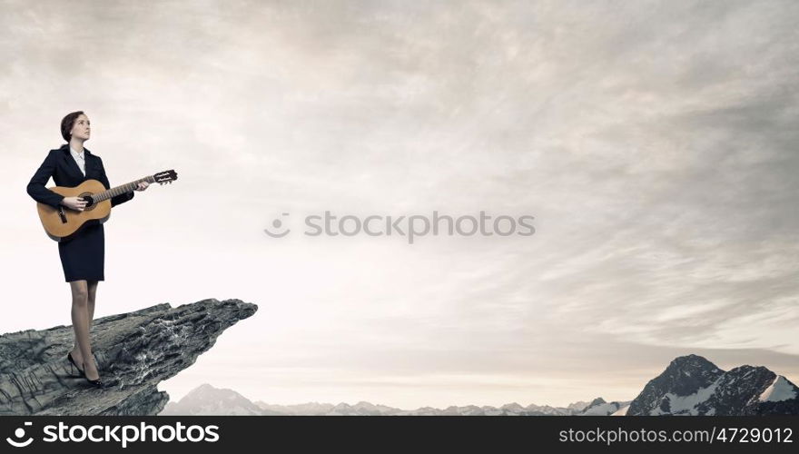 Businesswoman playing acoustic guitar. Cheerful businesswoman standing on rock edge and playing acoustic guitar