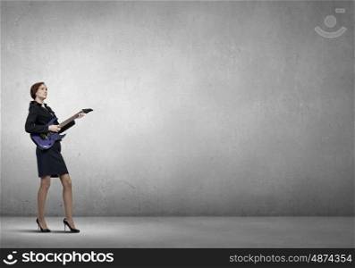 Businesswoman playing guitar. Cheerful businesswoman playing electric guitar on cement background