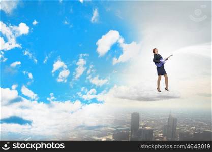 Businesswoman playing guitar. Cheerful businesswoman standing on cloud and playing electric guitar