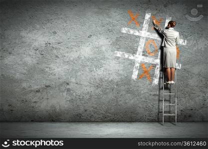 Businesswoman playing tictactoe on wall standing on ladder