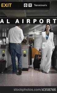 Businesswoman pulling her luggage and a mid adult man standing near a check-in machine at an airport