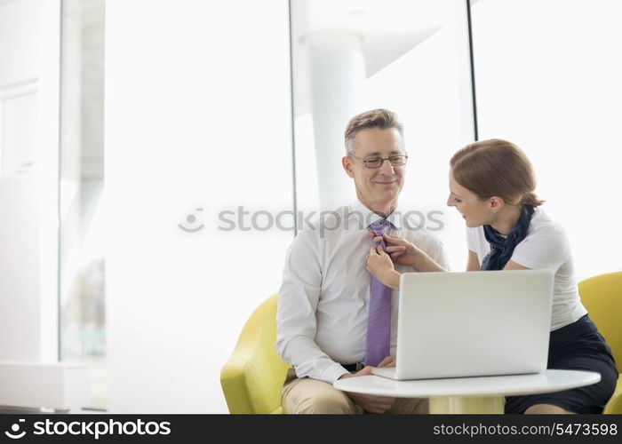 Businesswoman putting on tie to male colleague at lobby