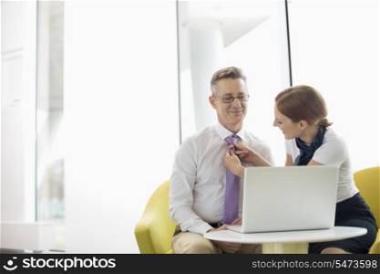 Businesswoman putting on tie to male colleague at lobby