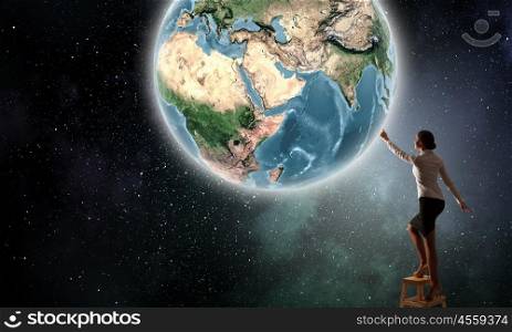 Businesswoman reaching Earth planet . Businesswoman standing on chair and reaching Earth planet. Elements of this image are furnished by NASA