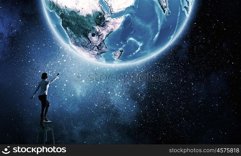 Businesswoman reaching Earth planet . Businesswoman standing on chair and reaching Earth planet. Elements of this image are furnished by NASA
