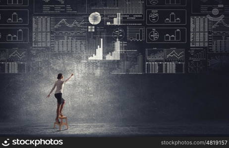 Businesswoman reaching idea. Back view of businesswoman standing on chair and reaching infographs on wall