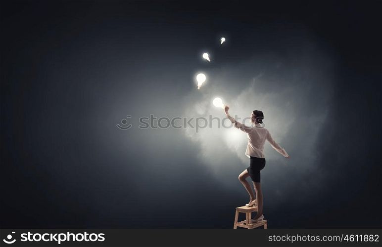 Businesswoman reaching idea. Back view of businesswoman standing on chair and reaching light bulb