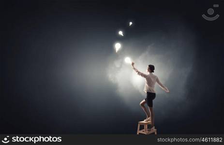 Businesswoman reaching idea. Back view of businesswoman standing on chair and reaching light bulb