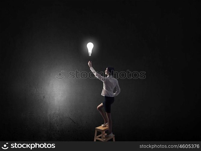 Businesswoman reaching light bulb. Back view of businesswoman standing on chair and reaching light bulb