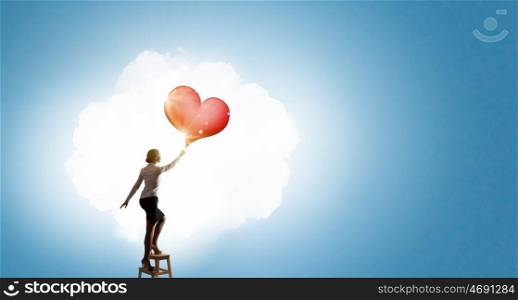Businesswoman reaching love . Businesswoman standing on chair and reaching red heart