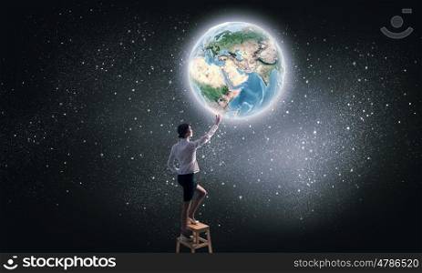 Businesswoman reaching planet in sky. Businesswoman standing on chair and reaching Earth planet. Elements of this image are furnished by NASA